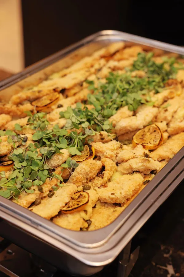 A chafing dish of crispy mains topped with herbs and lemon