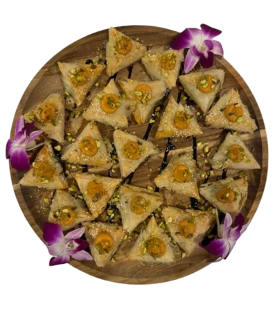 A platter of triangular pastries garnished with pistachios and orchids